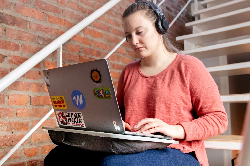 A person using a lap desk to work on their laptop while they are sitting in the middle of a staircase.