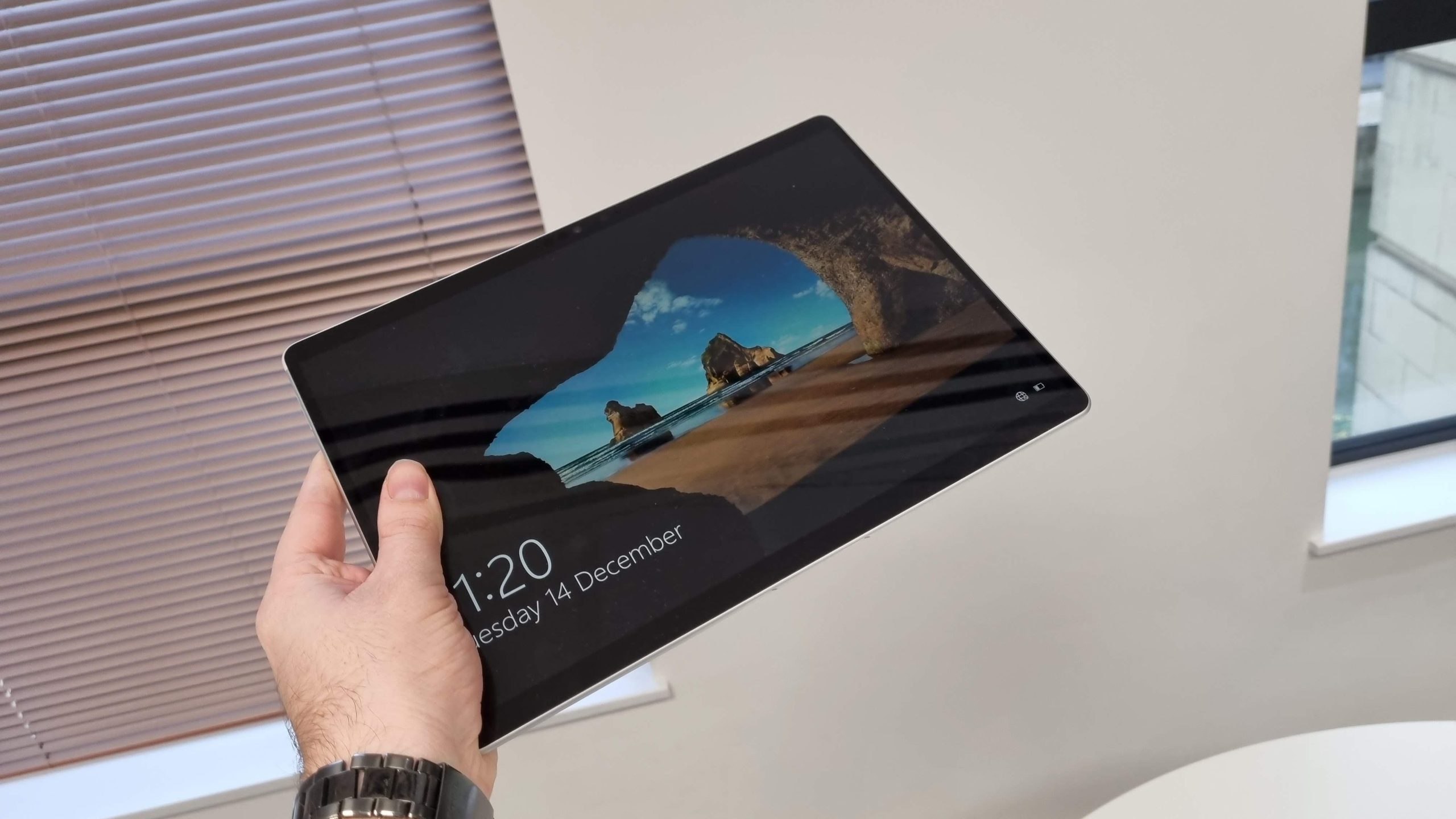 Someone holding a Microsoft Surface Pro 8 tablet in the air, open to its lock screen.